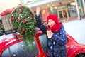 Happy young model girl with hot beverage in hands waves to someone comming. Girl stay near fashion red car ready for shoping