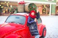 Happy young model girl with hot beverage in hands waves to someone comming. Girl stay near fashion red car ready for shopping