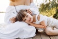 Happy young mom and child girl sitting near lake, pond. Mother and daughter smiling while spending free time outdoors Royalty Free Stock Photo