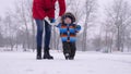 Happy young mother with a beautiful baby are walking in a winter park in snowy weather