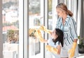 Happy young mother cleaning windows with her daughter using a squeegee. Smiling parent cleaning, completing housework