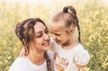 Happy young mother cuddles with her daughter in the summer on the field of rape. Happiness with family