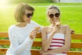 Happy young mother and cute daughter of a teenager in a city park eating ice cream, talking and laughing Royalty Free Stock Photo