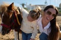 Happy young mother and daughter admiring together a pony horse. Family engaging in outdoors activities with little child