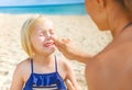 Happy young mother and daughter on beach applying SPF