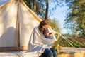 Happy young mother embracing her toddler girl with a blanket while sitting near canvas tent Royalty Free Stock Photo