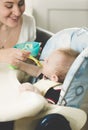 Happy young mother feeding her baby in highchair from spoon Royalty Free Stock Photo