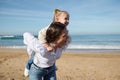 Happy young mother giving piggyback ride to her little daughter, enjoying walk together on the sandy beach Royalty Free Stock Photo