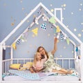 Happy young mother and her adorable daughter looking up and showing something interesting while sitting on bed Royalty Free Stock Photo