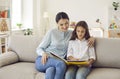 Happy young mother and her child sitting on the couch and reading a book together Royalty Free Stock Photo