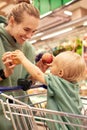 Happy young mother with her cute daughter in shopping trolley walking around supermarket. Beautiful mom and little Royalty Free Stock Photo