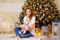 Happy young mother with her little baby girl sitting near Christmas tree on the floor in living room Royalty Free Stock Photo