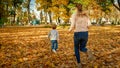 Happy young mother with her little son running on fallen yellow leaves in autumn park Royalty Free Stock Photo