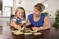 Happy young mother and her sweet and beautiful little daughter playing card game at home kitchen smiling and having fun together Royalty Free Stock Photo