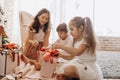 Happy young mother and her two charming daughters in nice dresses sit on the carpet and open New Year`s gifts in the