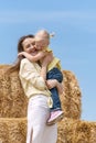 Happy young mother holds her little daughter in her arms against the background of haystack and blue sky. Countryside holidays Royalty Free Stock Photo