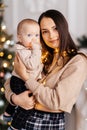 A happy young mother holds her little son in her arms against the backdrop of a beautifully decorated New Year tree Royalty Free Stock Photo
