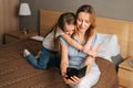 Happy young mother hugging to preschool daughter together browsing and surfing internet on mobile phone, chatting on Royalty Free Stock Photo