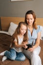 Happy young mother hugging to preschool daughter together browsing and surfing internet on mobile phone, chatting on Royalty Free Stock Photo