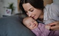 Happy young mother kissing her newborn baby girl, lying on sofa indoors at home. Royalty Free Stock Photo