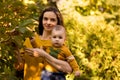 Happy young mother playing with baby in autumn park with yellow maple leaves. Family walking outdoors in autumn. Little boy with h Royalty Free Stock Photo