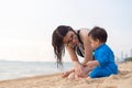 Happy young mother smiling and looking at her little baby boy playing sand on tropical beach vacation at summer time. people Royalty Free Stock Photo