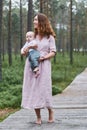 A happy young mother with a young son in her arms walks along a wooden path in a pine forest on a summer day Royalty Free Stock Photo