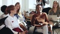 Happy young multiethnic business women sit together listening to corporate seminar laughing at modern office conference.