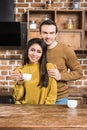 happy young multiethnic couple embracing and smiling at camera while drinking coffee Royalty Free Stock Photo