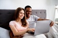 Happy young multinational couple relaxing on bed, using laptop, watching movies together Royalty Free Stock Photo