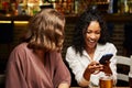 Happy young multiracial friends in casual clothing smiling while using mobile phone at restaurant Royalty Free Stock Photo