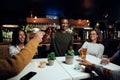 Happy young multiracial group of friends in casual clothing toasting with drinks over table Royalty Free Stock Photo