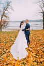 Happy young newly married couple posing on autumn lakeshore full of orange leaves Royalty Free Stock Photo