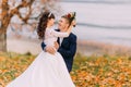 Happy young newlywed bridal couple posing on autumn lakeshore full of orange leaves Royalty Free Stock Photo