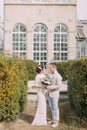 Happy young newlyweds embracing near the old beige house with columns and big vintage windows. Romantic wedding in Paris Royalty Free Stock Photo