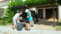 Happy young newlyweds packing their heavy baggage in the trunk of a black SUV. Royalty Free Stock Photo