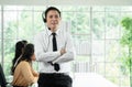 Happy young operator man working with headset smile and standing in front of group of Asian employee work in telemarketing Royalty Free Stock Photo