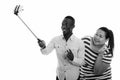 Happy young overweight Asian woman and young African man as couple taking selfie together with phone on selfie stick Royalty Free Stock Photo