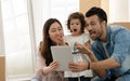 Happy young parents Caucasian father and Asian mother holding tablet with little kid girl show exciting face Royalty Free Stock Photo