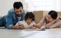Happy young parents Caucasian father and Asian mother lying on floor and play drawing with little kid girl at home. Royalty Free Stock Photo