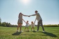 Happy young parents spending time together, holding hands in circle with their two little kids, boy and girl in green Royalty Free Stock Photo