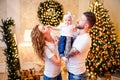 Happy young parents standing near Christmas tree in living room while holding little nice baby girl Royalty Free Stock Photo