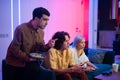 Happy young people playing video games on console while sitting on couch in front of tv. Man advice his friend in a game Royalty Free Stock Photo