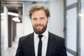 Happy young positive male office worker manager, wearing black suit and tie, smiling at camera, standing on the Royalty Free Stock Photo