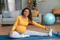 Happy young pregnant african american woman with big belly doing exercises and practicing yoga in living room