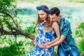 Happy and young pregnant couple hugging in nature on sunset. New family expecting baby in scenic place near river in summertime. Royalty Free Stock Photo