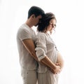 Happy young pregnant couple in white pajamas hugging and holding belly bump in morning light. Stylish pregnant family, mom and dad Royalty Free Stock Photo