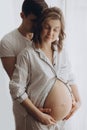 Happy young pregnant couple in white pajamas hugging and holding belly bump in morning light. Stylish pregnant family, mom and dad Royalty Free Stock Photo