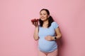 Happy young pregnant woman in blue casual t-shirt, holding bowl with fresh ripe organic strawberries, isolated on pink Royalty Free Stock Photo