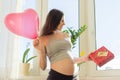 Happy young pregnant woman with gift box and heart balloon Royalty Free Stock Photo